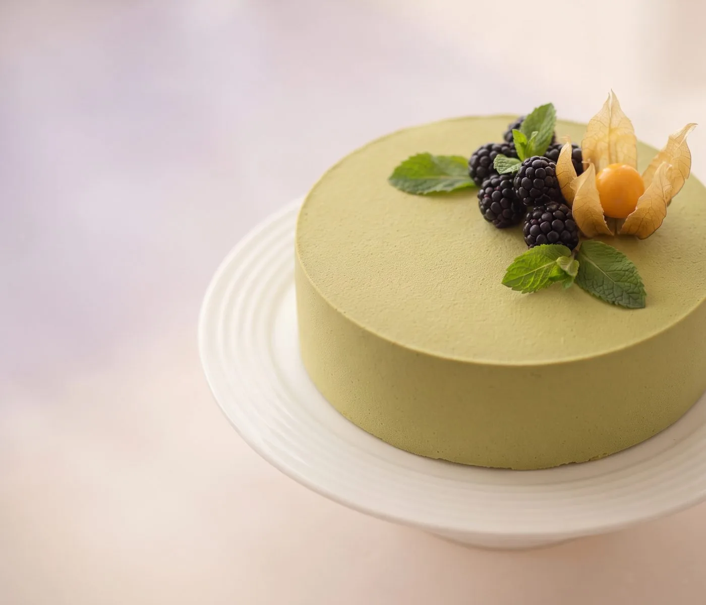 Runde Mousse-Torte mit pistaziengrünem Überzug, oben mit Brombeeren, Minze und Physalis belegt